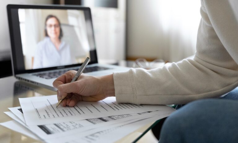 Image d'une personne qui écrit sur une feuille en visio sur un ordinateur - Luxury Hotelschool