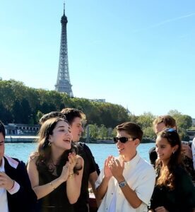 Photo d'étudiants dans un bateau qui tapent dans leur main avec la tour Eiffel en fond - Luxury Hotelschool