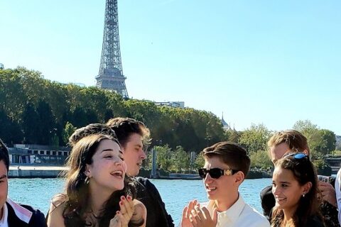 Photo d'étudiants dans un bateau qui tapent dans leur main avec la tour Eiffel en fond - Luxury Hotelschool